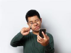 Een man kijkt met een vergrootglas naar een smartphone.