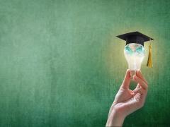 Een hand houdt een peertje (lamp) vast. De lamp heeft een afstudeerhoedje op.