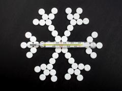 Pillen zijn neergelegd in de vorm van een sneeuwvlokje. Er ligt een thermometer bovenop.