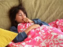 Een kind ligt op de bank onder een deken. 