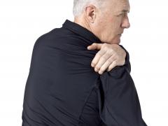 Een man legt zijn hand op zijn rechterschouder.