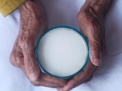 Een paar oude handen is gevouwen om een kop melk.