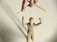 Een hand houdt een houten marionet vast.