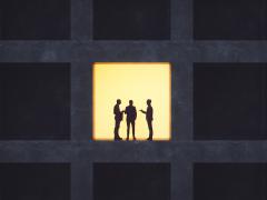 Drie silhouetten in gesprek in een verlicht raam van een verder donker gebouw.