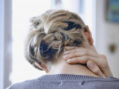 Een vrouw zit voorover gebogen met haar hand in haar nek.