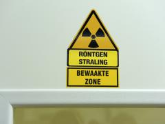 Gele waarschuwingsstickers met de teksten 'röntgenstraling" en "bewaakte zone" boven een deurpost.