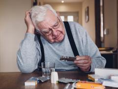 Een oudere man zit aan tafel en bekijkt een pillenstrip.