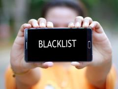 Iemand houdt een smartphone vast. Op het scherm staat het woord 'blacklist'.