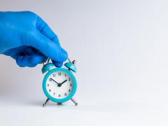 Een hand in een rubberen handschoen houdt een kleine wekker vast.