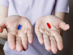 2 handen met in de ene hand een rode pil, in de andere een blauwe