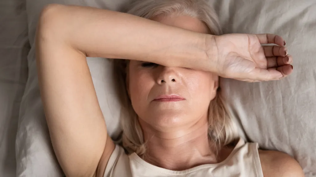 Een liggende vrouw die met haar arm haar ogen bedekt, wat een gevoel van vermoeidheid, hoofdpijn of rusteloosheid uitstraalt